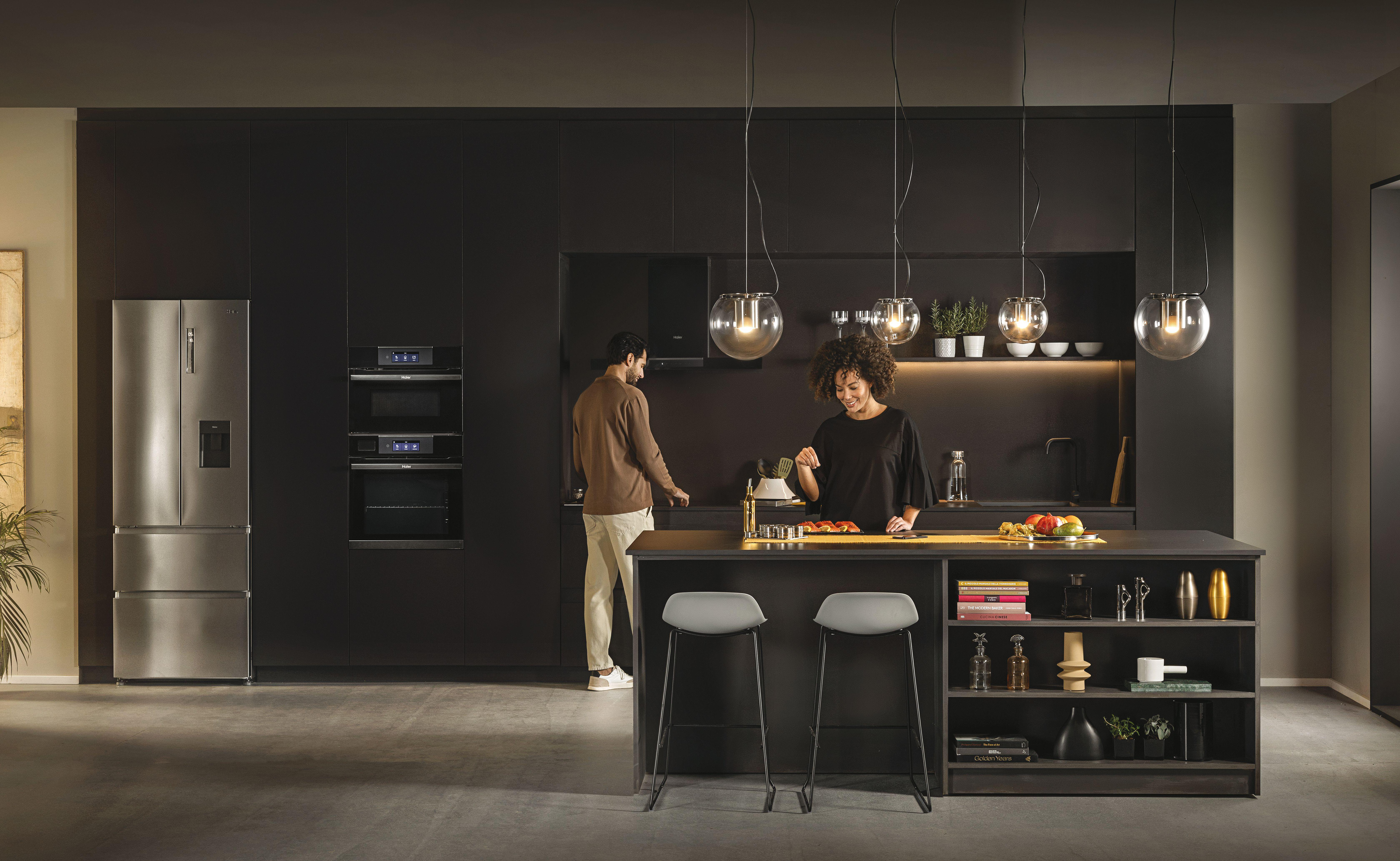 Ein Paar bereitet Essen in einer modernen Küche mit dunklen Schränken und einem Kühlschrank zu.