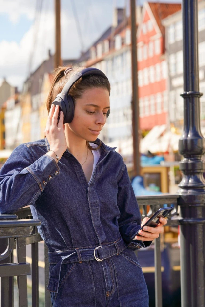Frau mit Kopfhörern, die Musik hört, hält ein Telefon, urbaner Hintergrund.