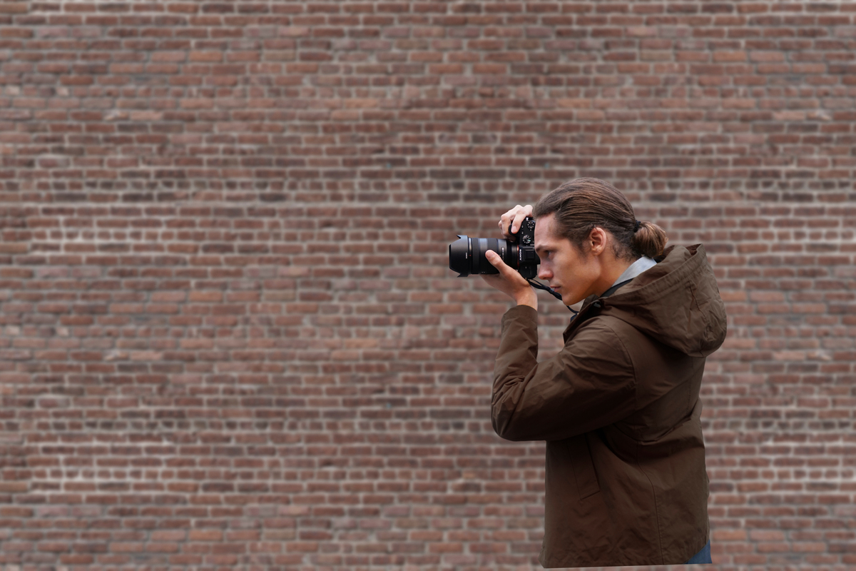 Un homme prenant une photo avec un appareil photo devant un mur de briques.