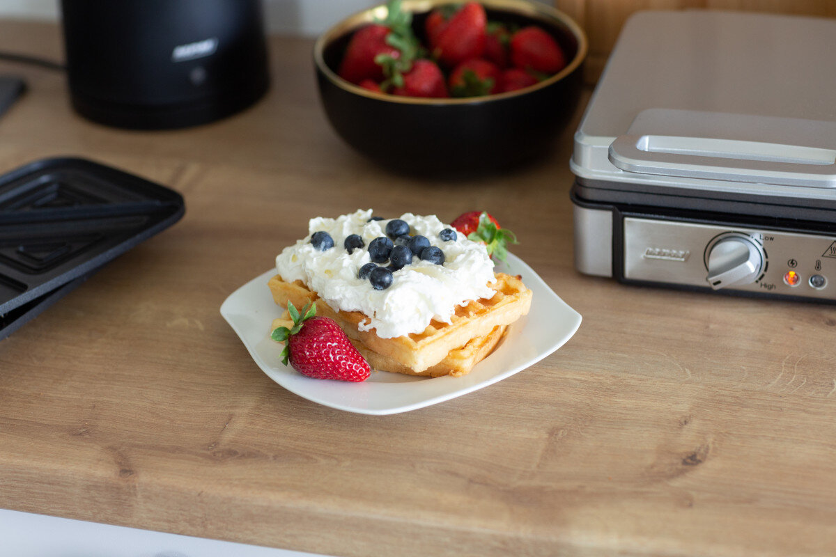 Gofry z bitą śmietaną i borówkami na talerzu, z truskawkami.