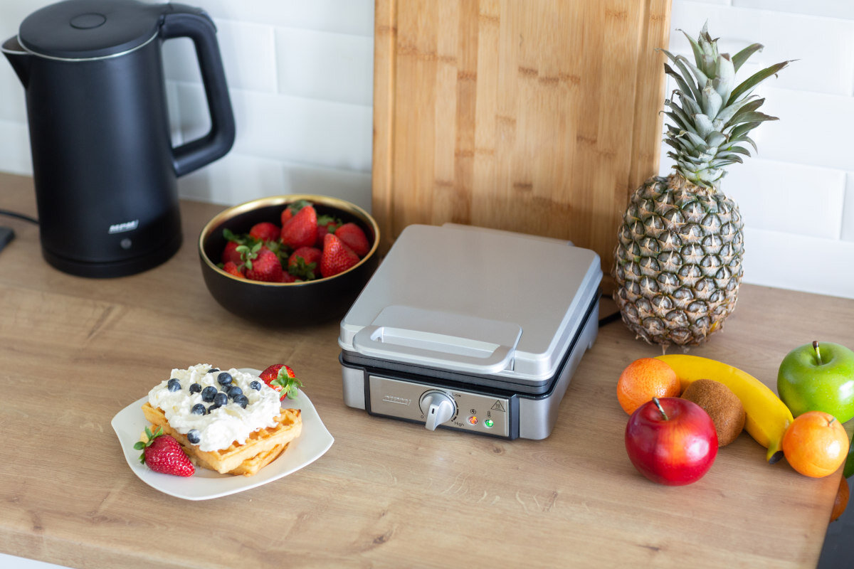 Gofry z owocami i gofrownica na drewnianej powierzchni. Czajnik czarny.