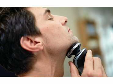 Mężczyzna goli szyję golarką elektryczną. Ma zamknięte oczy.