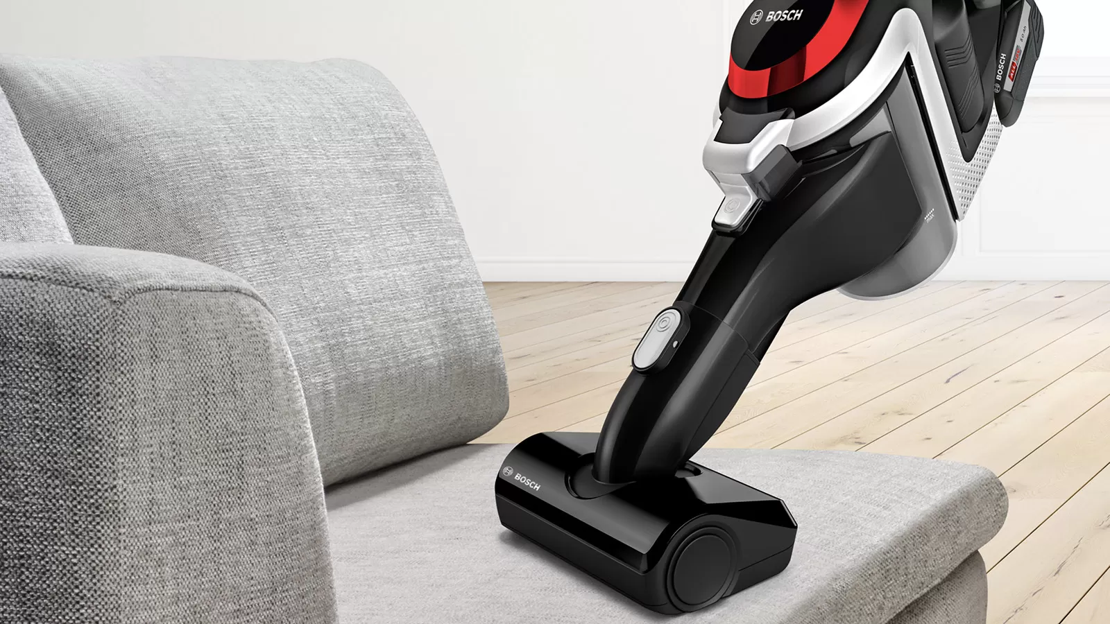 Czarny odkurzacz akumulatorowy Bosch na szarej poduszce obok sofy.
