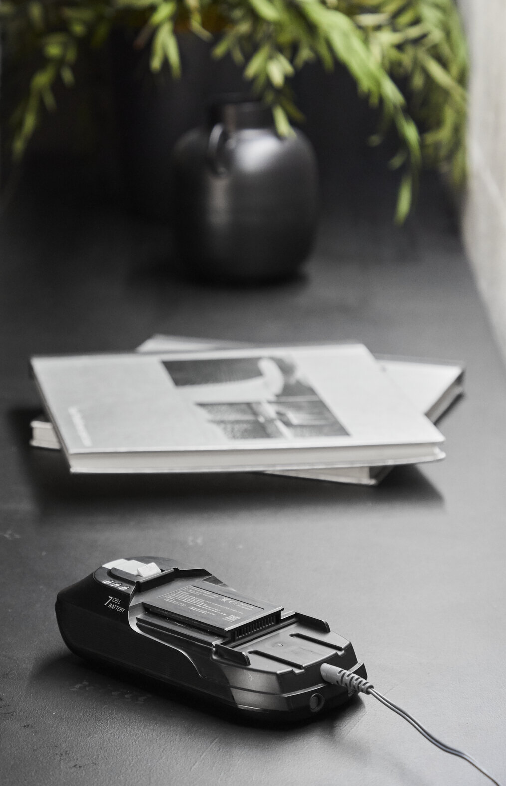 Czarny akumulator 7-ogniwowy podłączony kablem. Książki za nim.