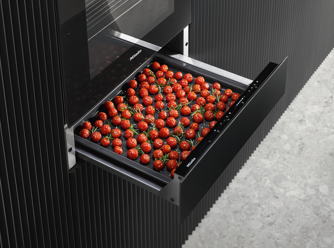 Ein Backblech mit vielen kleinen roten Tomaten und Rosmarin in einer Schublade.