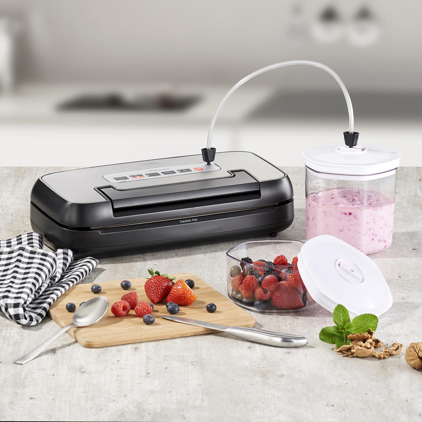 Vakuumierer, Behälter und Lebensmittel auf einem Tisch. Beeren, Minze und ein Schneidebrett.