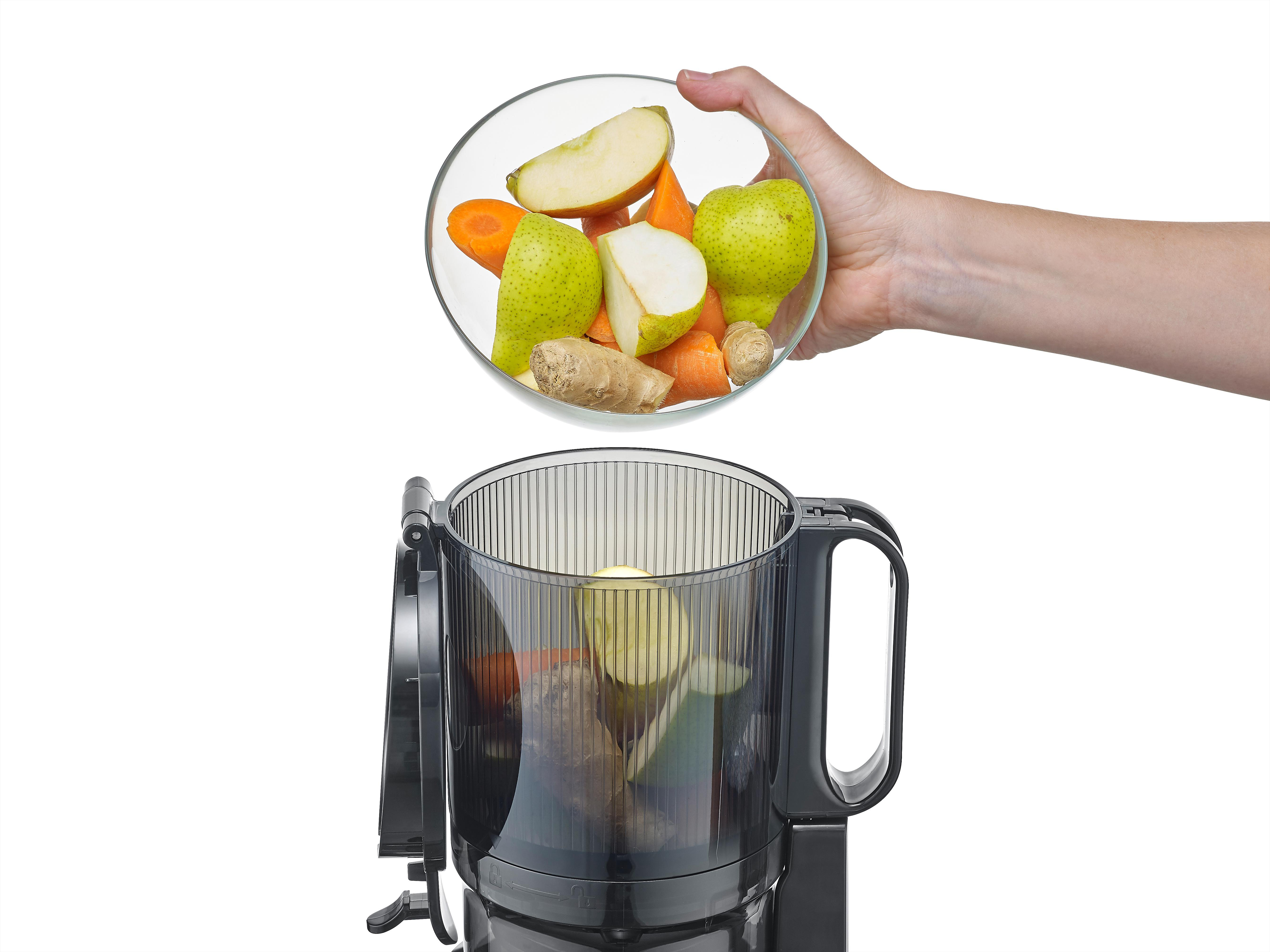 Eine Hand, die eine Glasschüssel mit geschnittenen Früchten über einem Food-Prozessor hält.