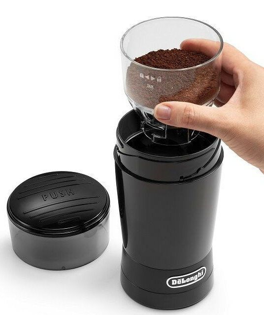 Osoba trzymająca młynek do kawy z zmieloną kawą w środku.