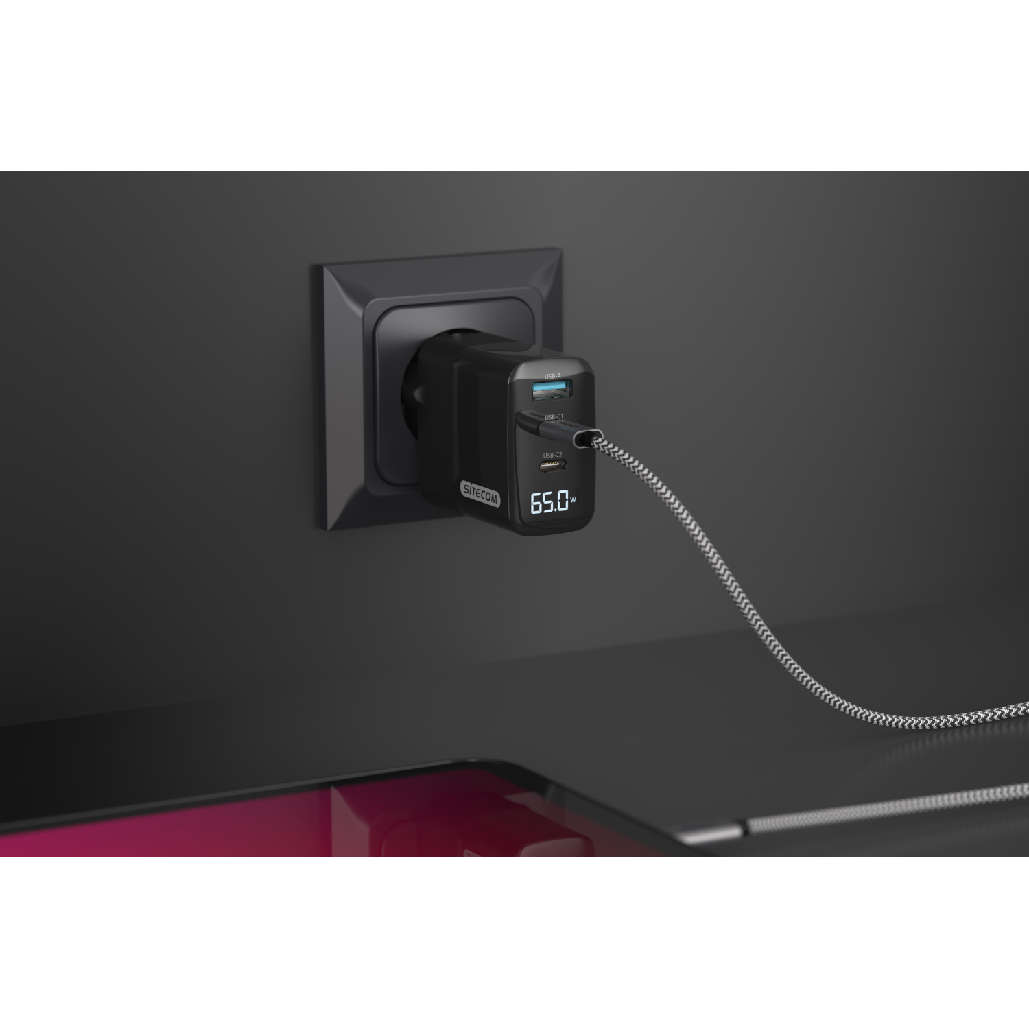 A black wall charger plugged into a dark grey outlet, charging a device with a cable.