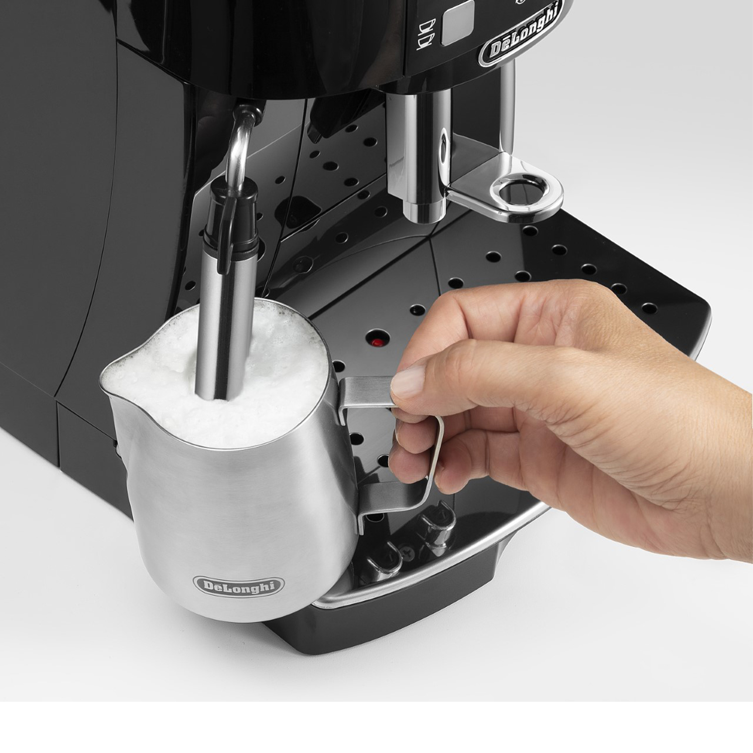 Una mano che versa il latte in un bricco in acciaio inox da una macchina da caffè.