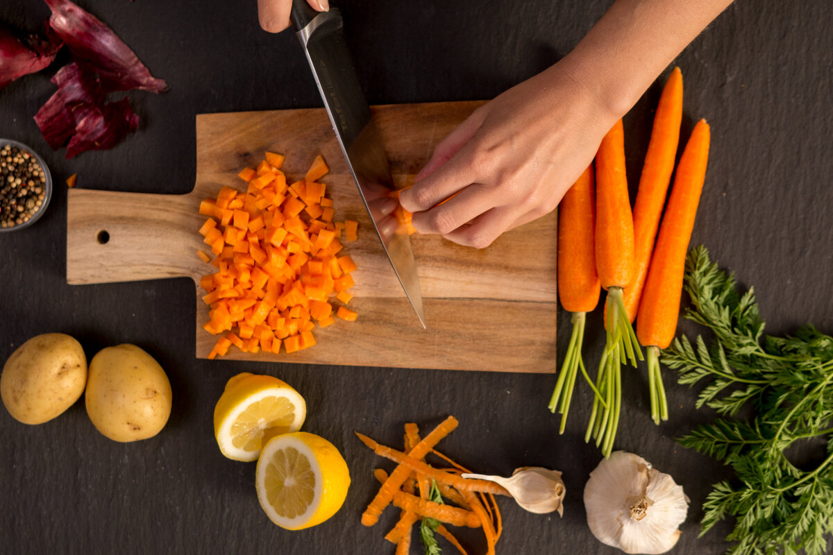 Widok z góry na osobę krojącą marchew na drewnianej desce z innymi składnikami.