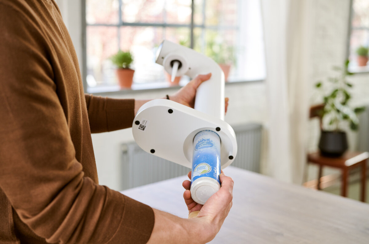 Osoba trzyma białe urządzenie, prawdopodobnie medyczne. Widoczny jest niebieski pojemnik.