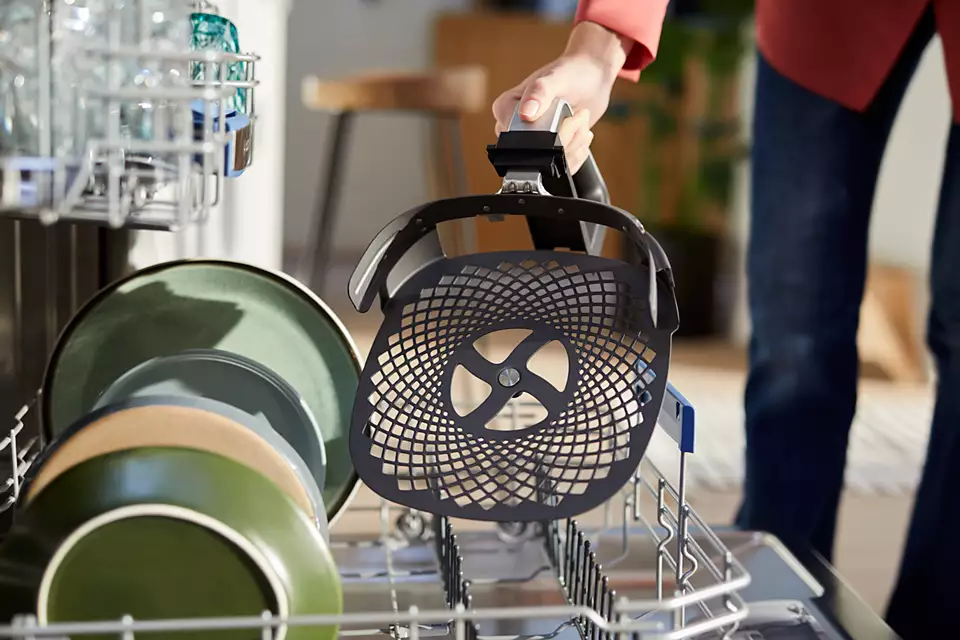Osoba wyjmująca czarny kosz frytkownicy powietrznej z półki zmywarki.
