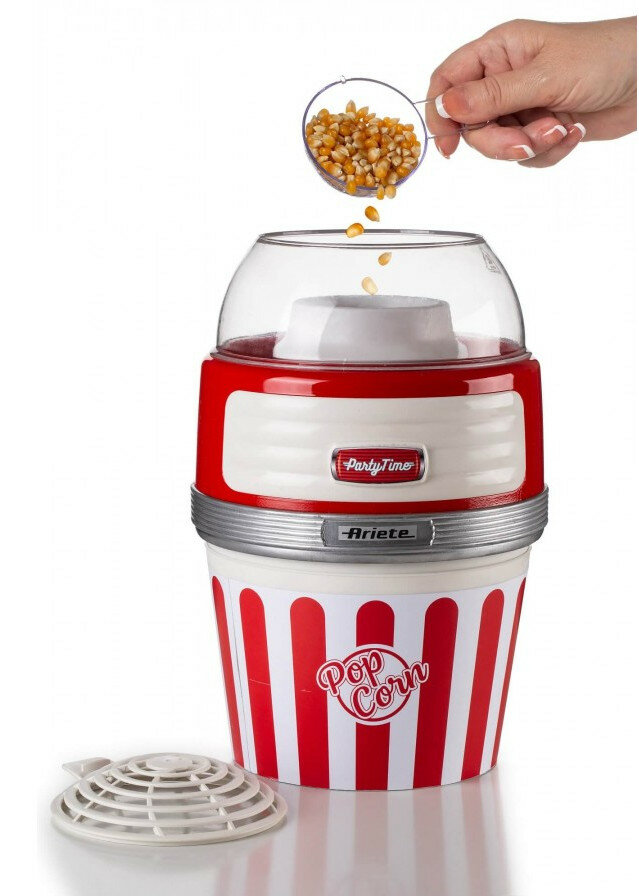 Ręka kobiety wsypuje ziarna popcornu do czerwono-białej maszyny do popcornu w paski.