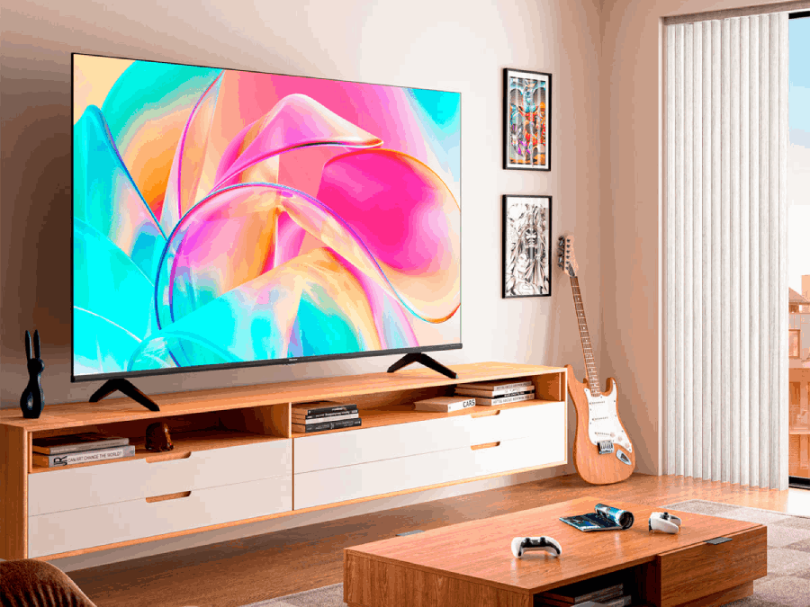 Salón con TV, barra de sonido y guitarra. Pantalla colorida, muebles de madera, luz brillante.