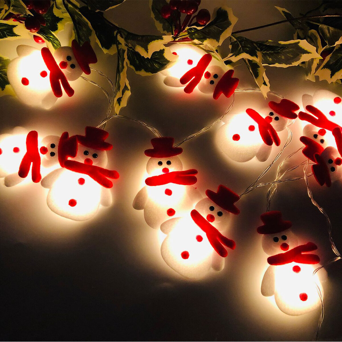 Światełka bożonarodzeniowe z małymi bałwankami w czerwonych szalikach i kapeluszach na ciemnym tle.