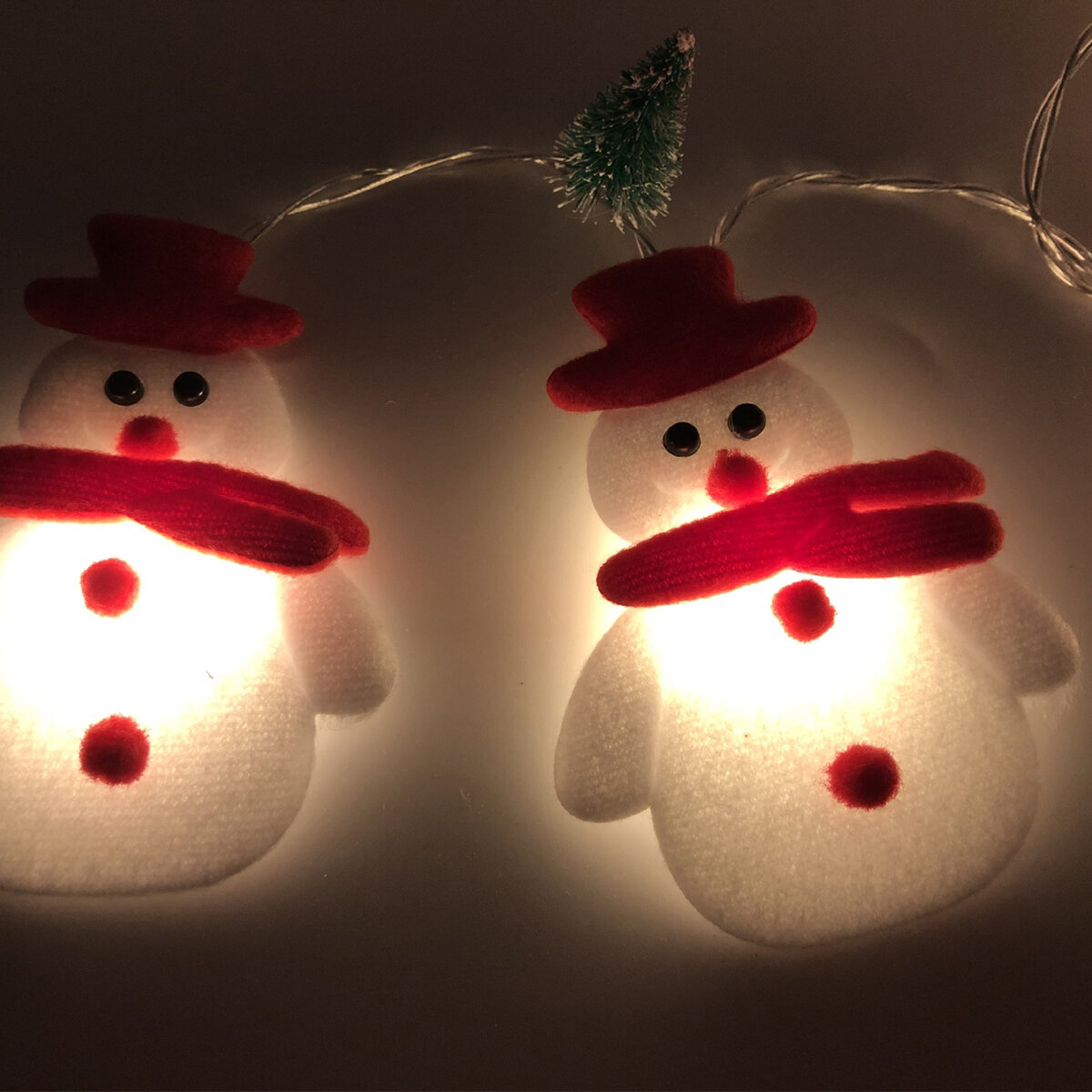 Dwa bałwanki lampki choinkowe z czerwonymi kapeluszami i szalikami na ciemnym tle.