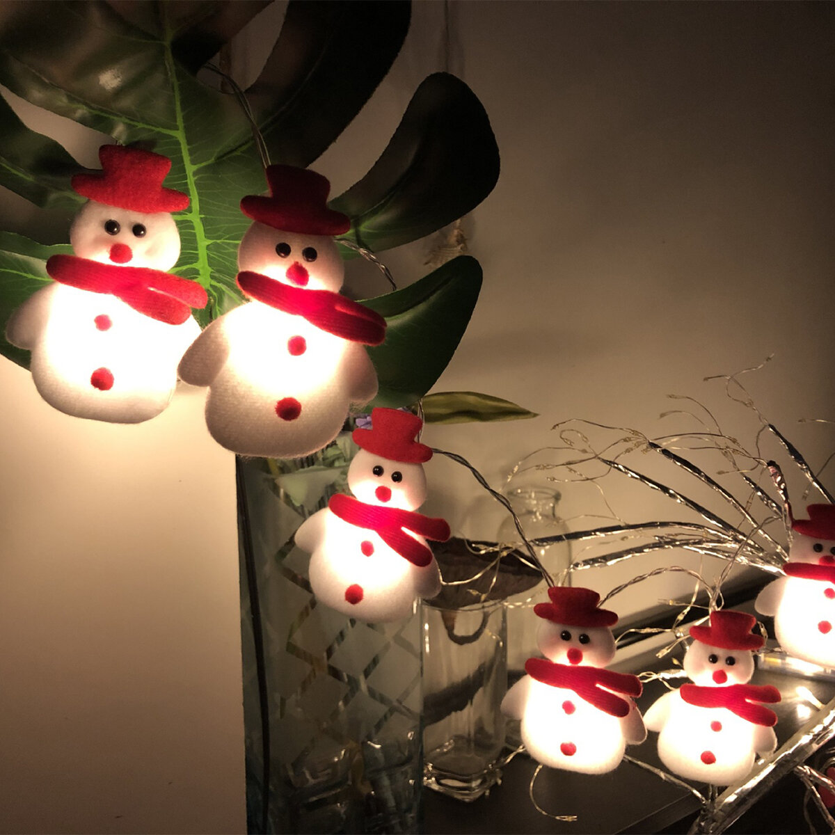 Szereg lampek w kształcie bałwanków, z ciemnym tłem i zielonymi liśćmi.