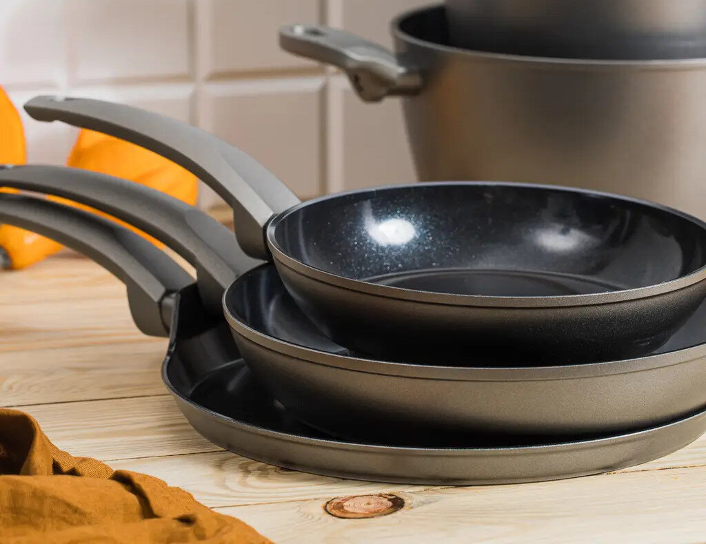 Zestaw trzech patelni nieprzywierających o różnych rozmiarach na drewnianej powierzchni.