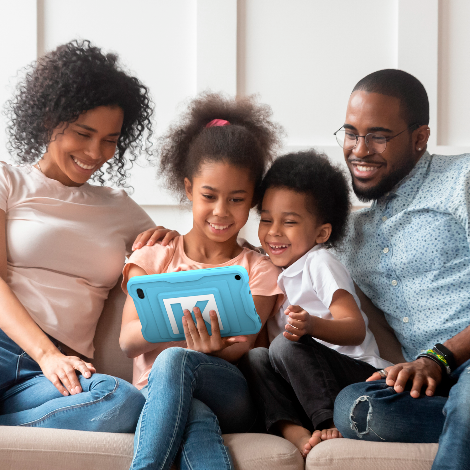A family of four, sitting on a couch, looking at a blue tablet. They are all smiling.