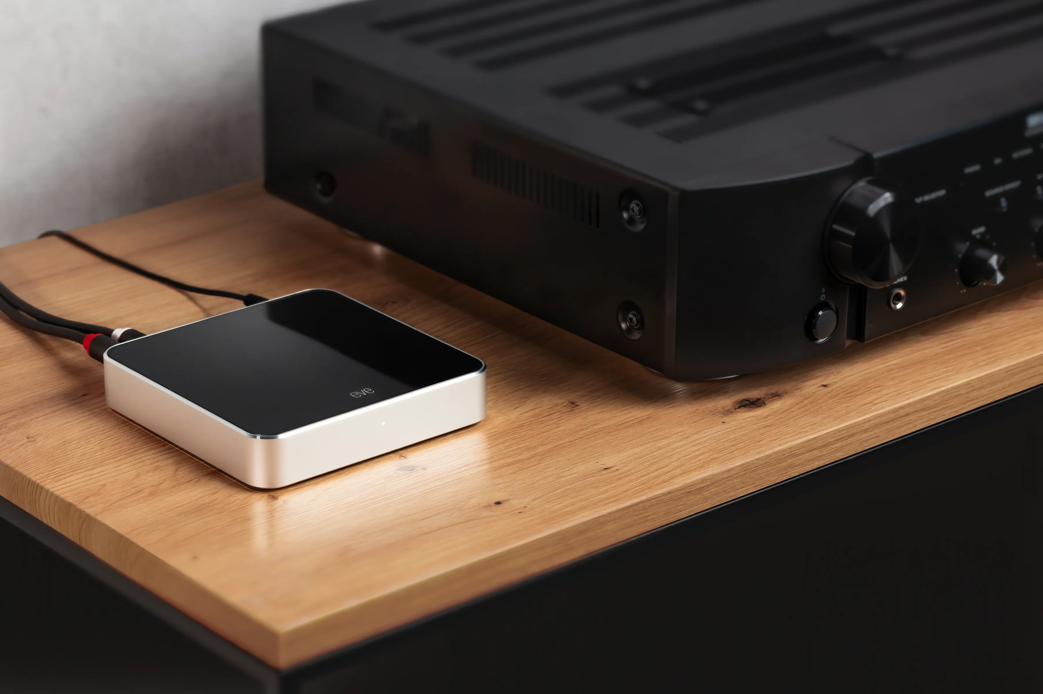 Un piccolo dispositivo audio nero su un tavolo di legno, collegato a un ricevitore nero.