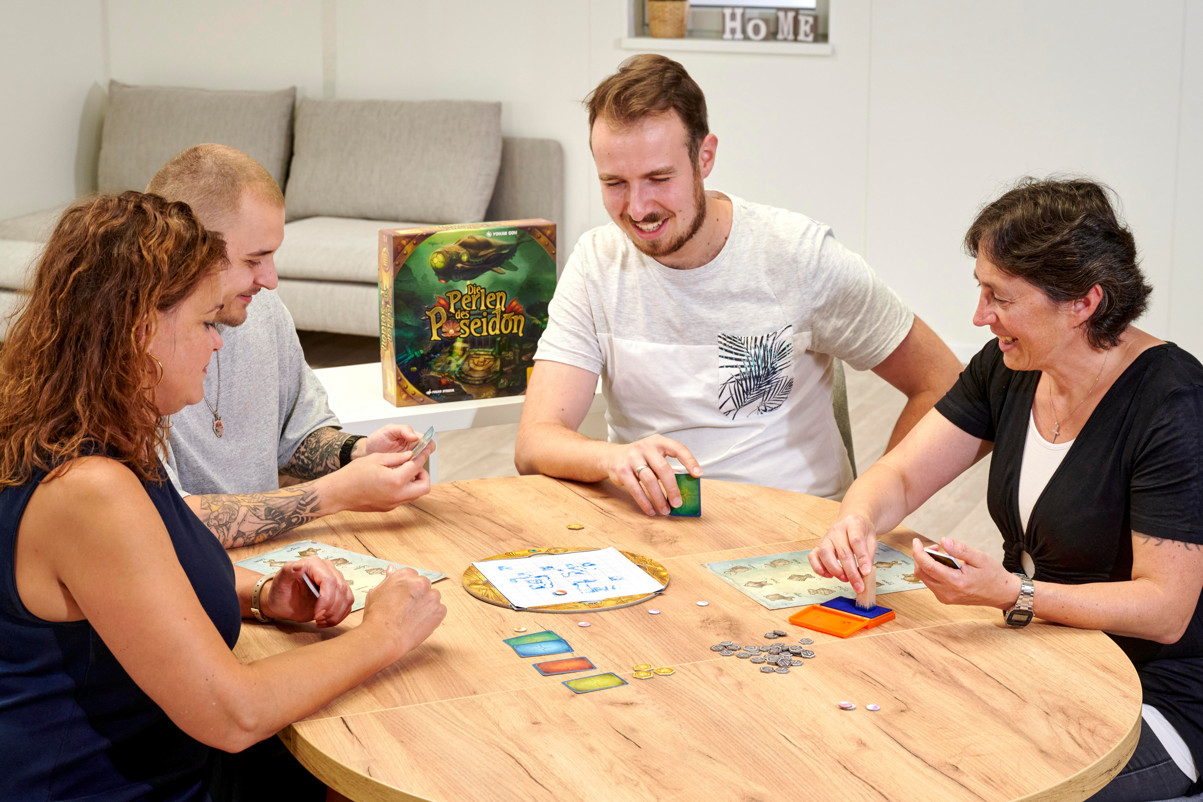 Vier Personen spielen ein Brettspiel an einem Holztisch. Die Spielbox ist sichtbar.