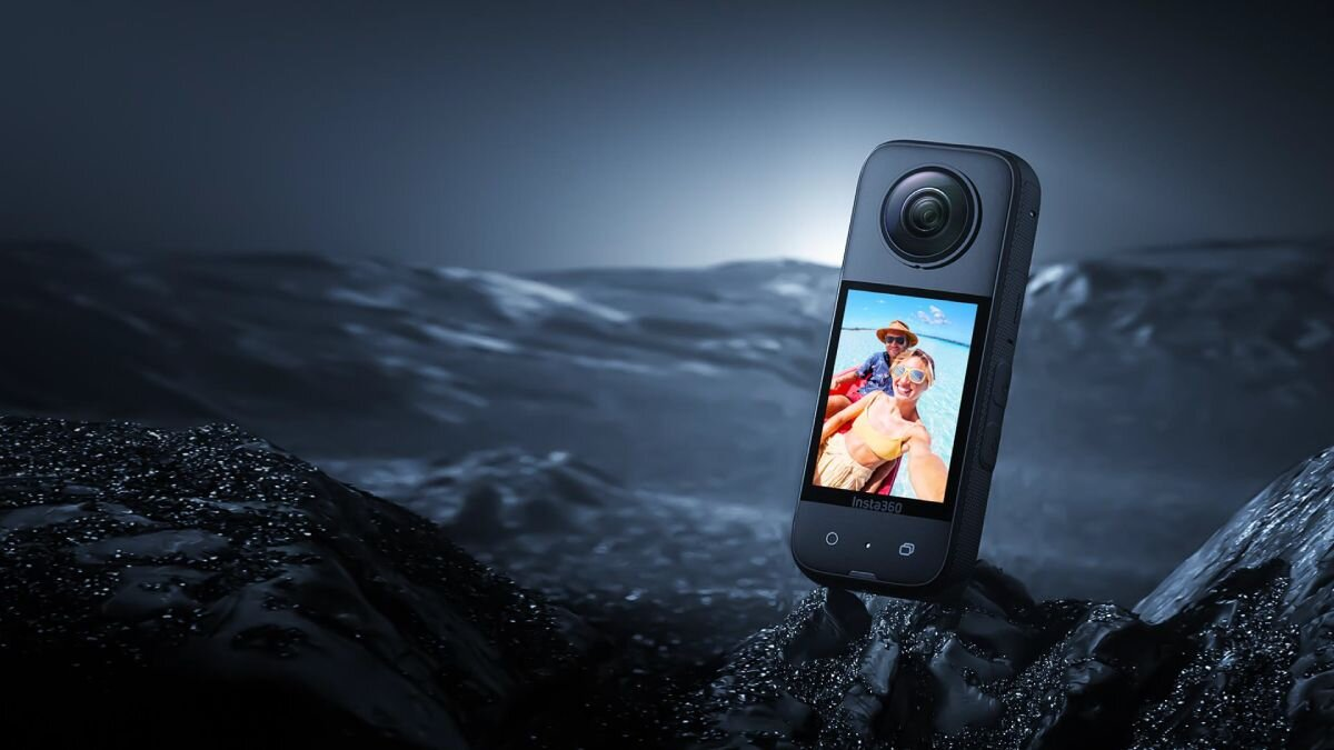 Kamera 360 z ekranem wyświetlającym zdjęcie dwóch osób na plaży. Ciemne tło.