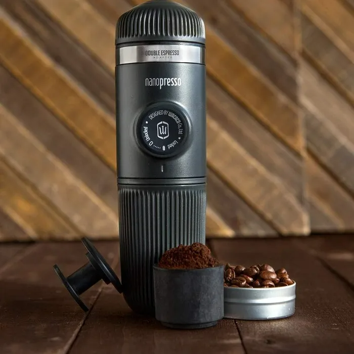 Egy fekete Nanopresso eszpresszó készítő, kávéőrleménnyel és babbal kis tartályokban.