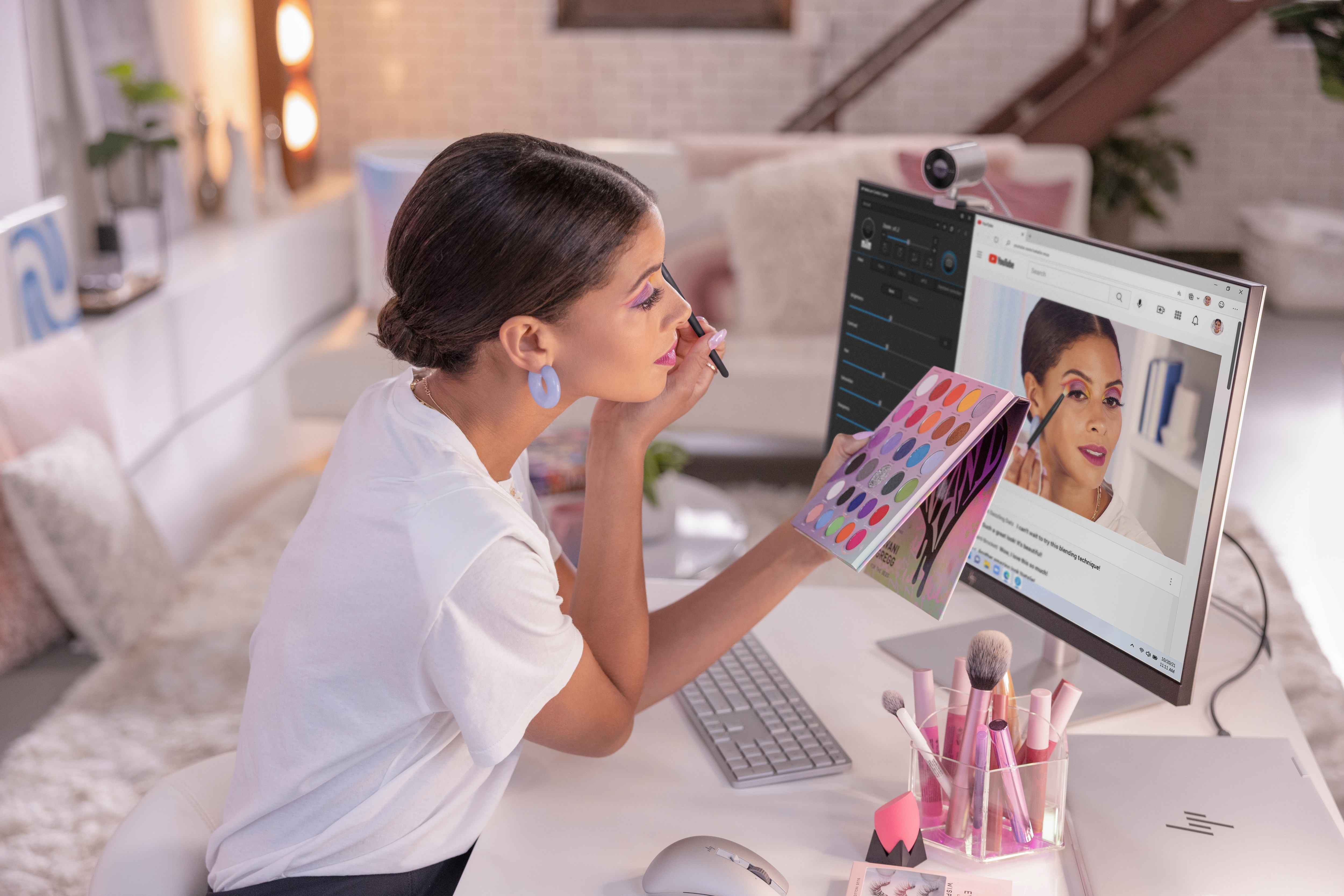 Eine Frau, die sich schminkt, während sie auf einen Computerbildschirm mit einem Make-up-Tutorial schaut.