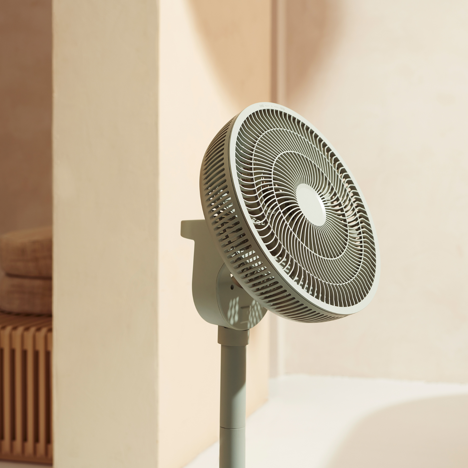 Een grijze ventilator op een standaard, schuin, in een neutrale kamer. Beige muren en een houten bijzettafel.