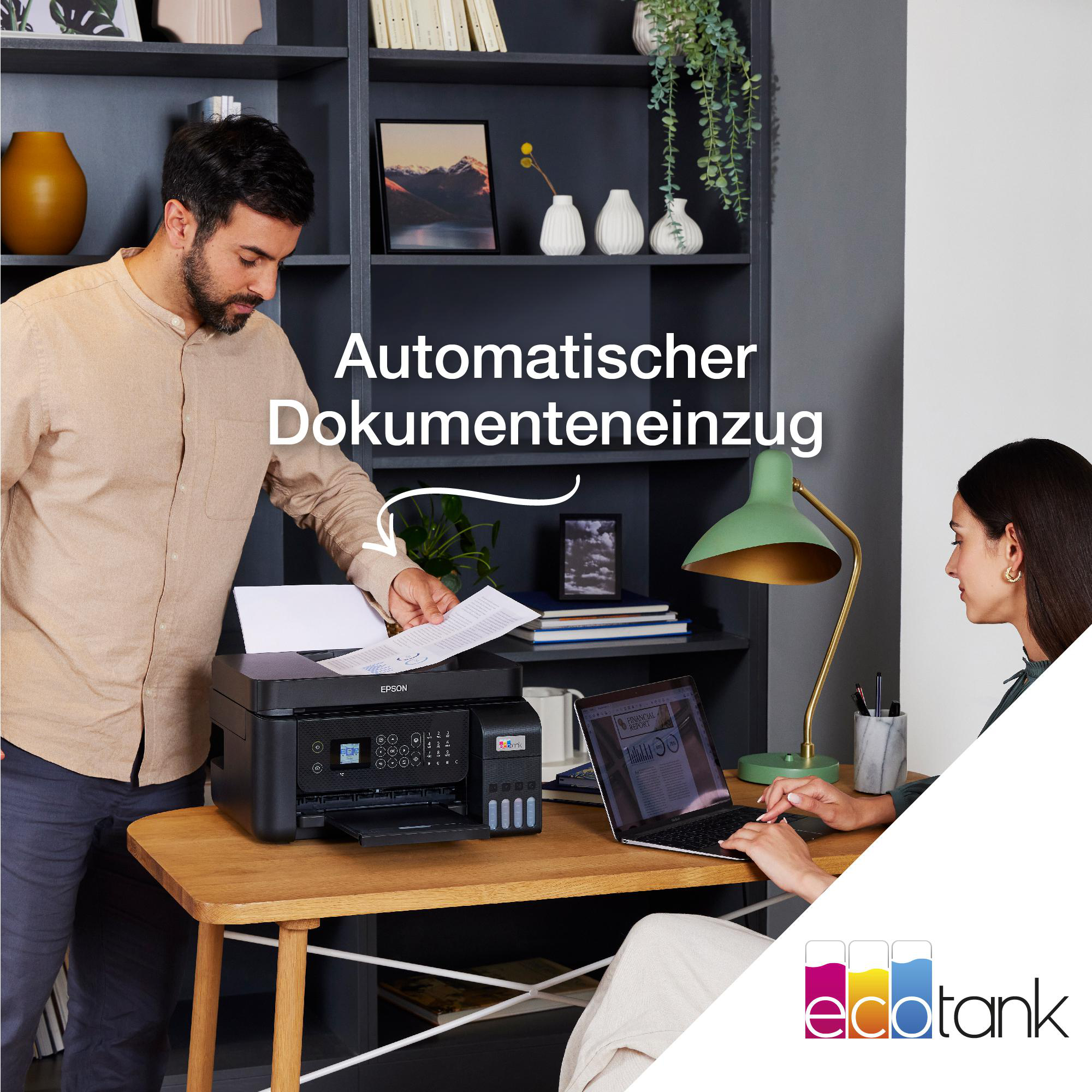 Ein Mann zeigt auf einen Drucker, während eine Frau an einem Laptop an einem Holztisch arbeitet.
