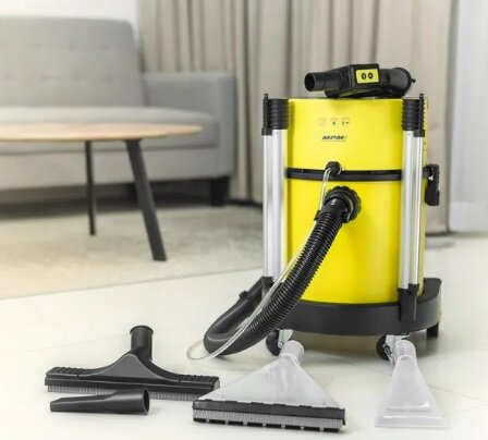 Żółty odkurzacz z akcesoriami. W tle sofa i stół.