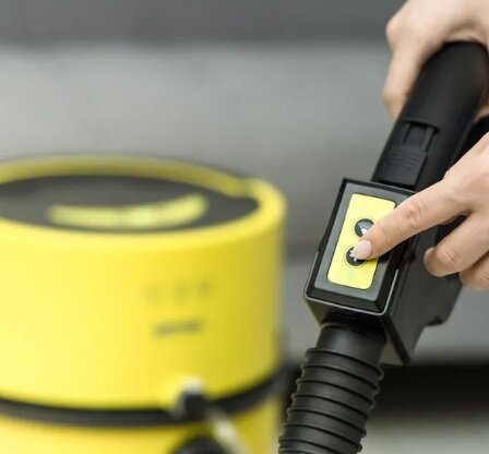 Dłoń osoby naciskająca przycisk na żółto-czarnym urządzeniu czyszczącym.