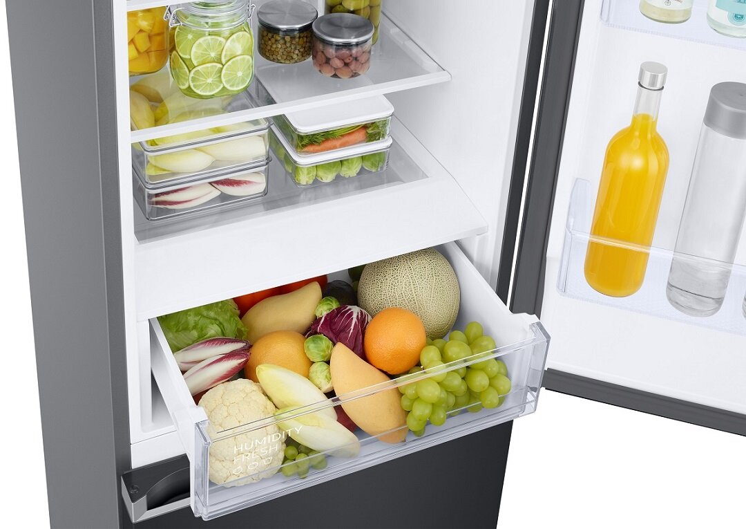 Wnętrze lodówki z owocami i warzywami w szufladzie oraz półkami z jedzeniem.