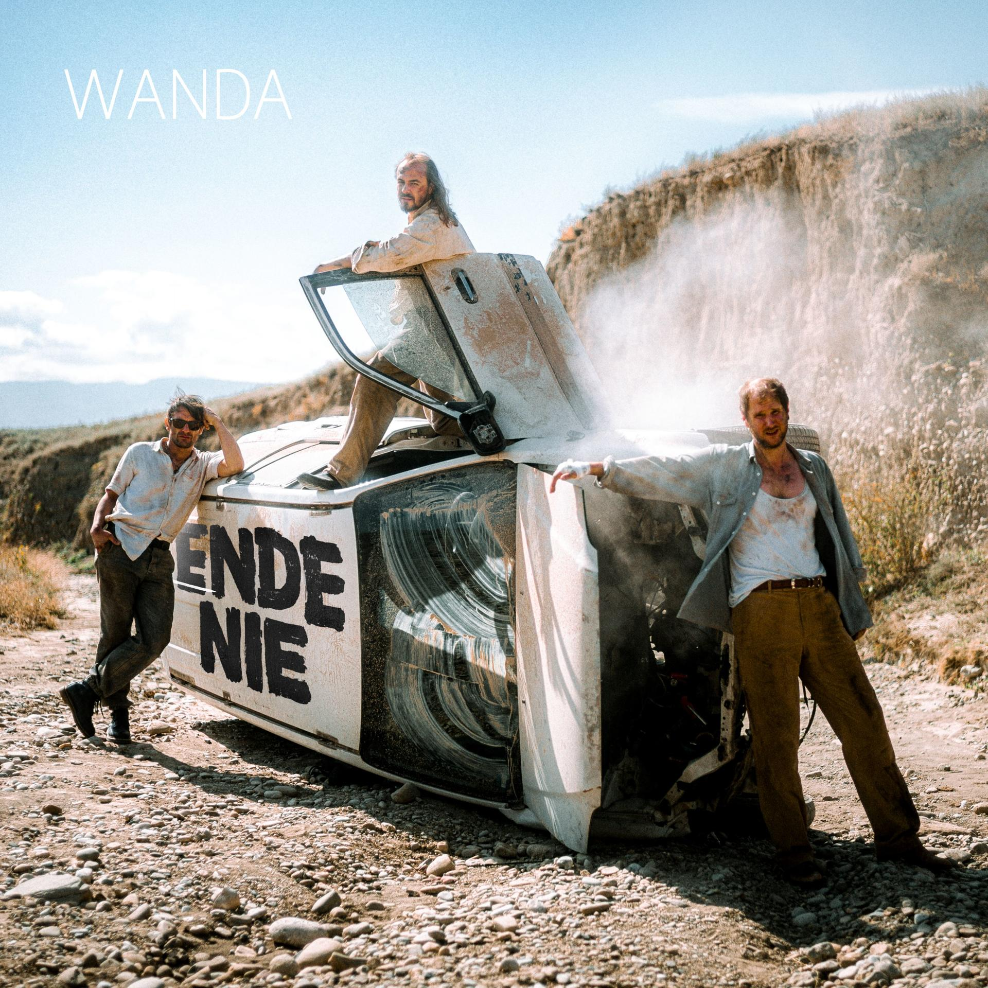 Albumcover: Bandmitglieder mit einem verunglückten Auto auf einer staubigen Straße mit Rauch.