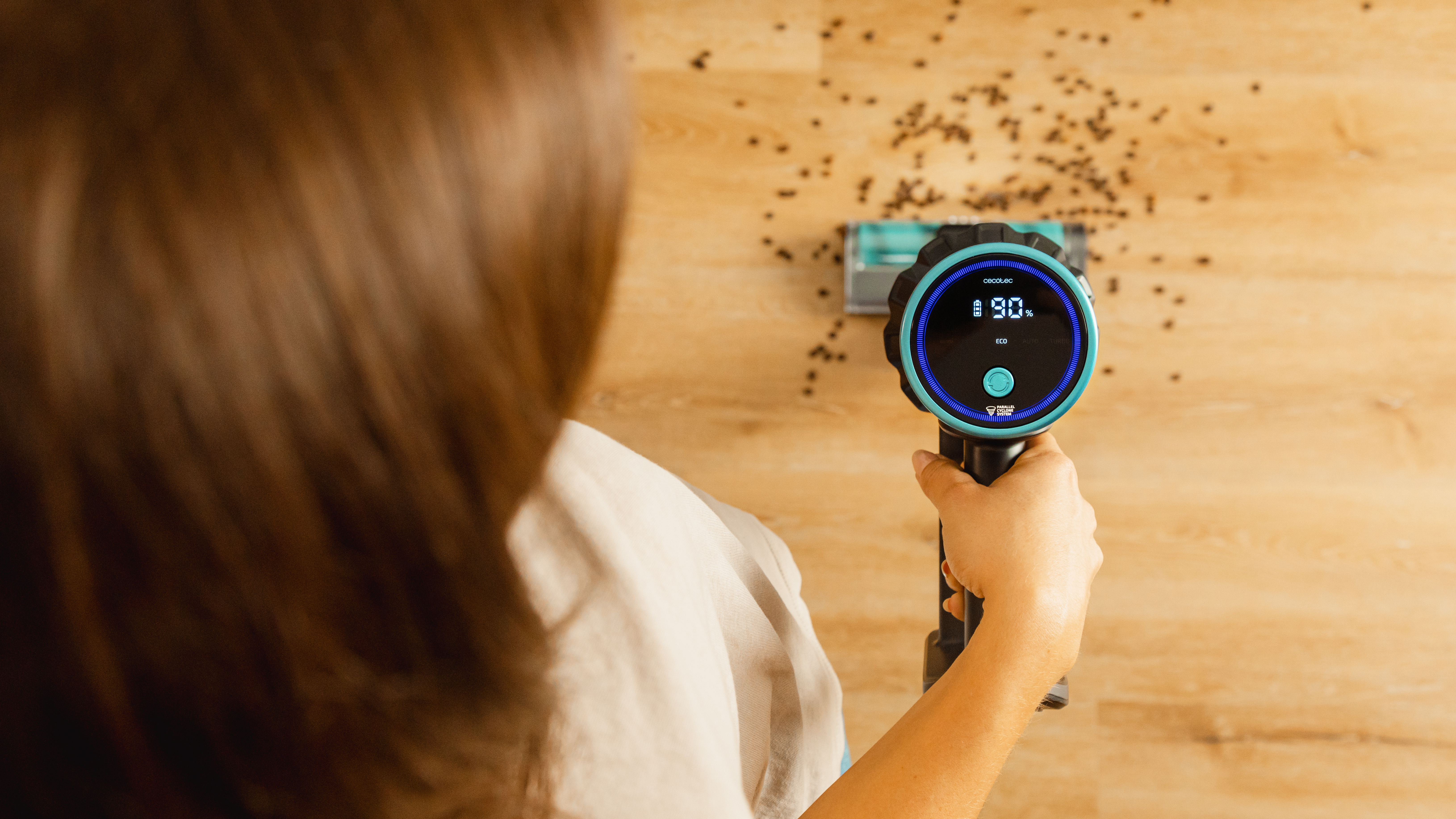 Una persona usando una aspiradora en un piso de madera. La aspiradora tiene una pantalla digital.