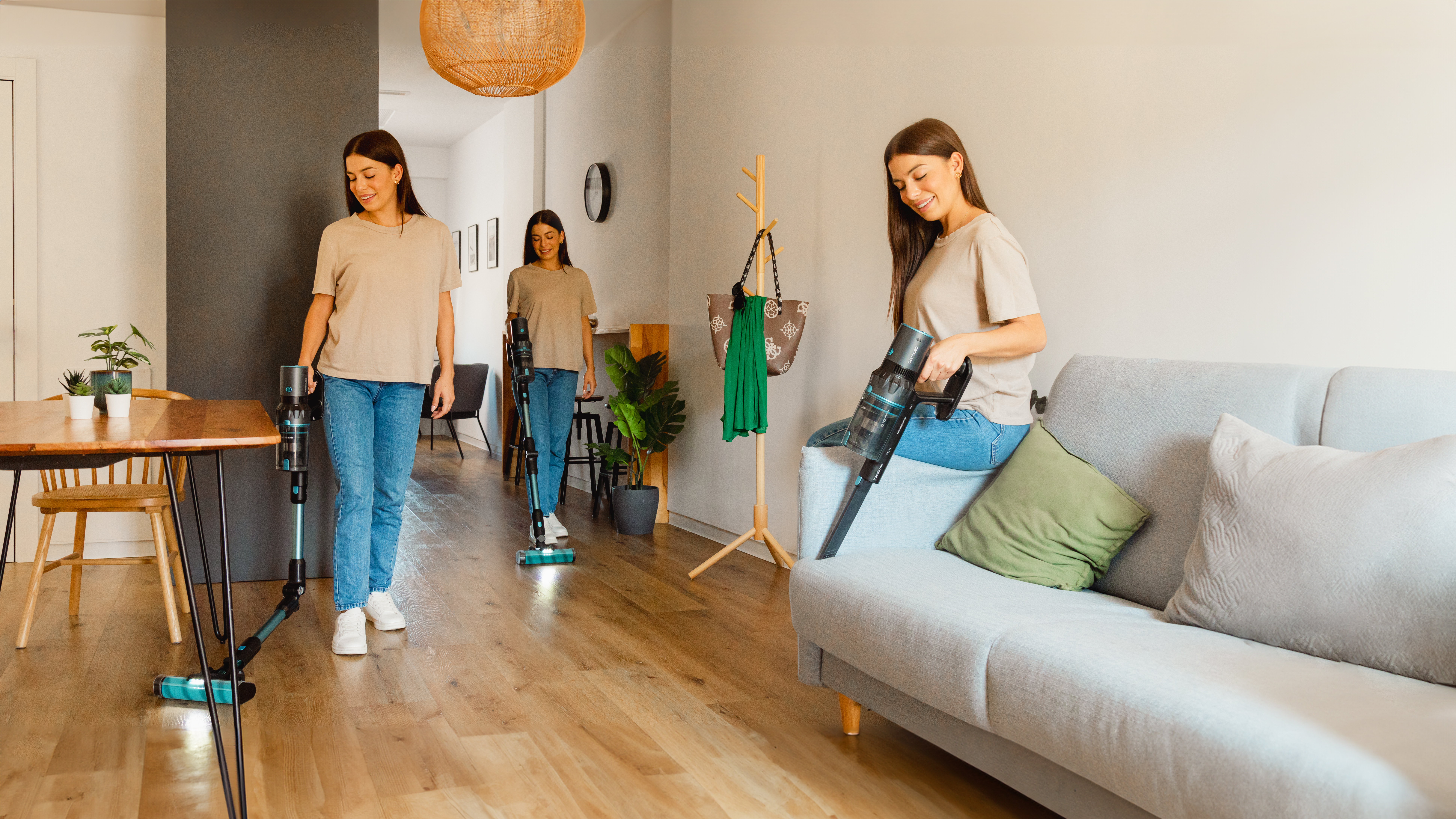 Tres mujeres aspirando una casa. Una usa aspiradora de mano en sofá. Suelo madera.