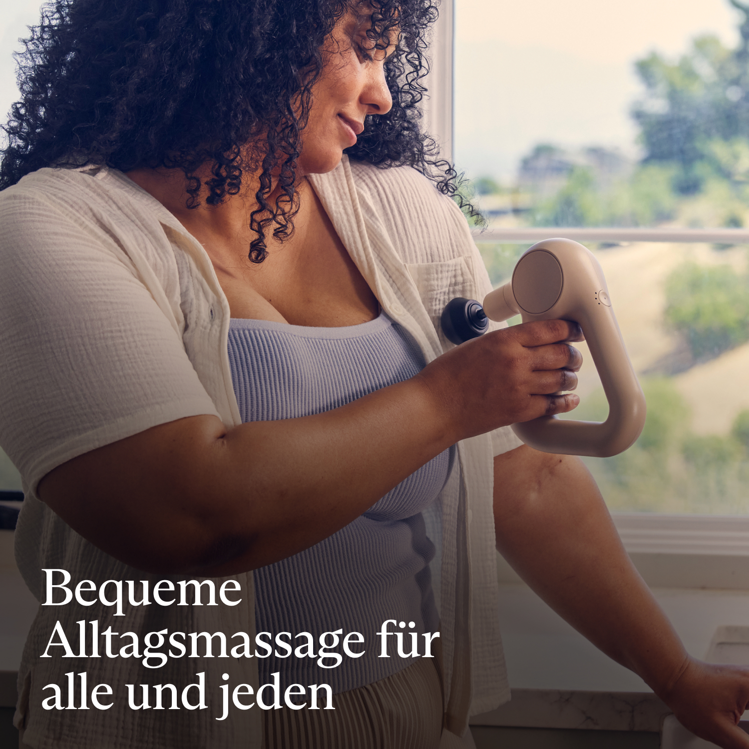 Eine Frau massiert ihren Arm mit einem Handmassagegerät in der Nähe eines Fensters.