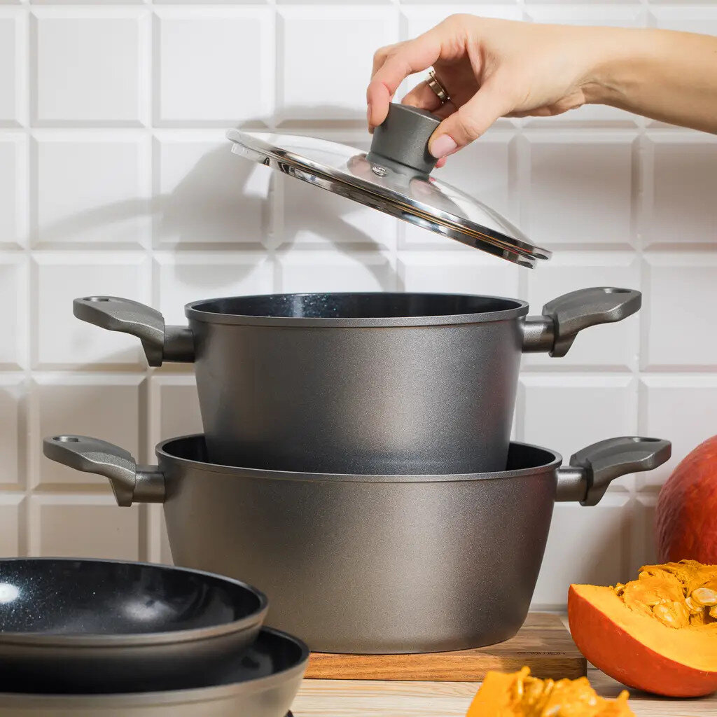 Kobieta zdejmuje pokrywkę z garnka. Dwa garnki i patelnia ułożone. Na scenie dynia.