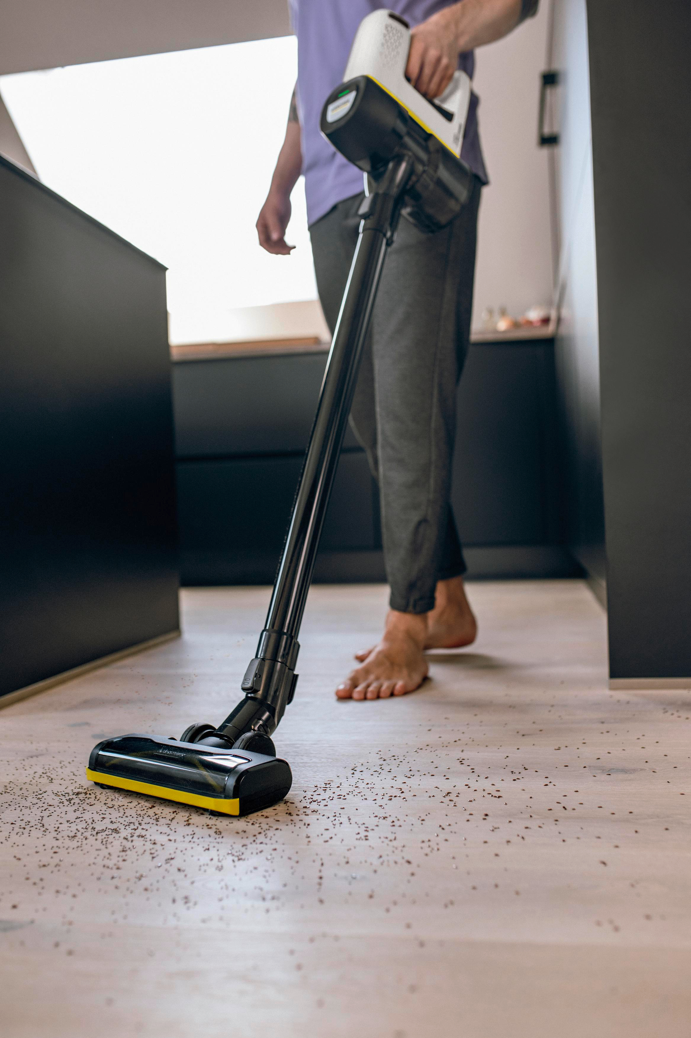 Eine Person saugt einen Holzboden mit einem schwarz-gelben Akku-Staubsauger.
