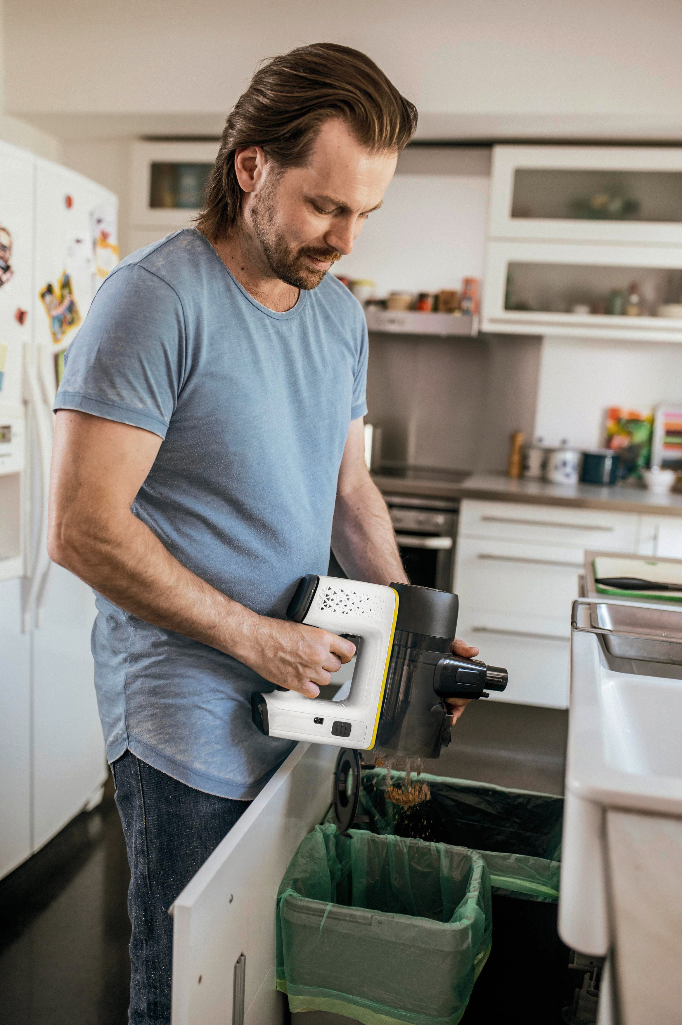 Ein Mann entleert einen weißen und gelben kabellosen Staubsauger in einen grünen Müllsack.