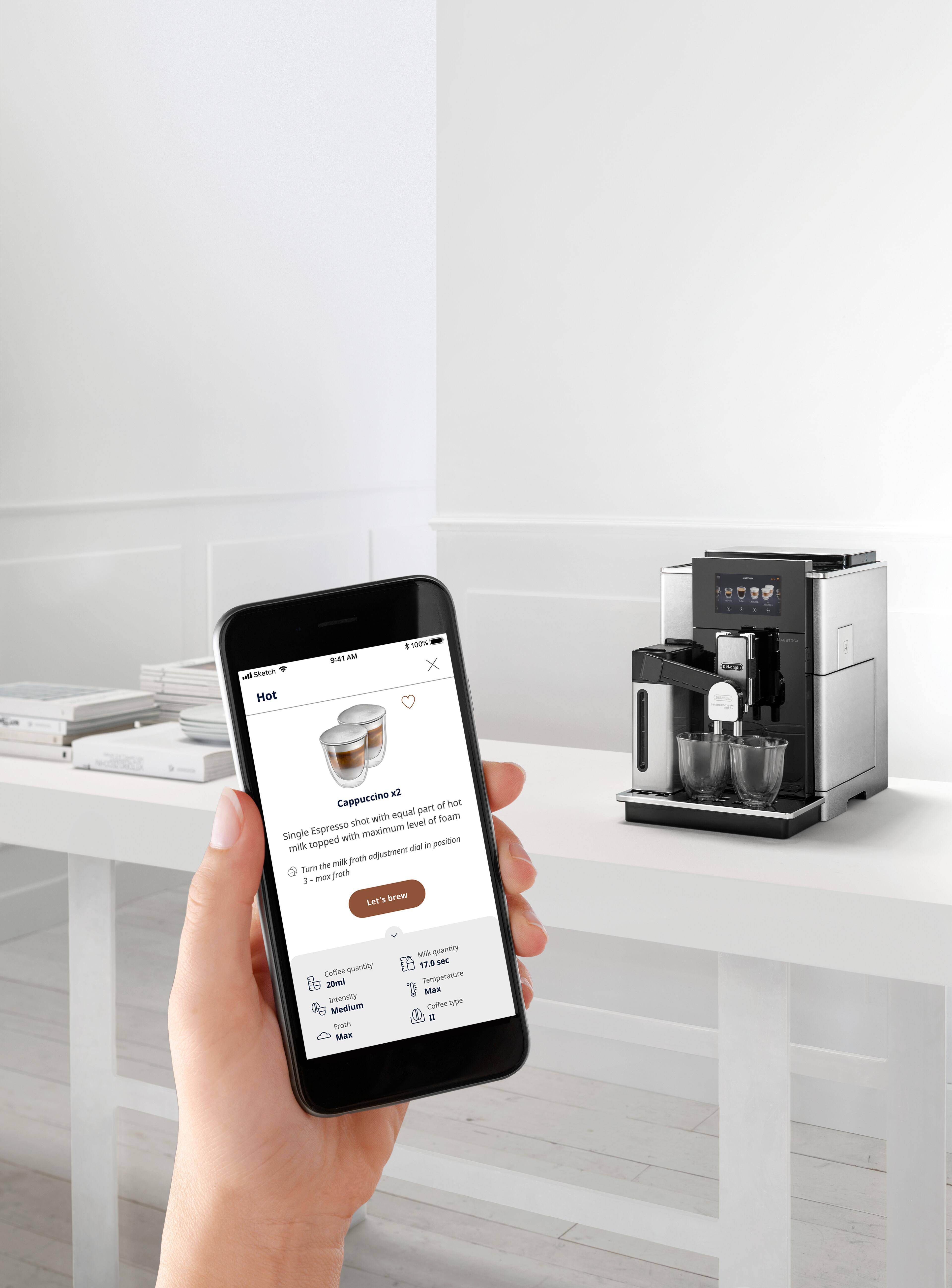 Eine Person hält ein Telefon, das die Cappuccino-Zubereitung auf einer Kaffeemaschine zeigt.