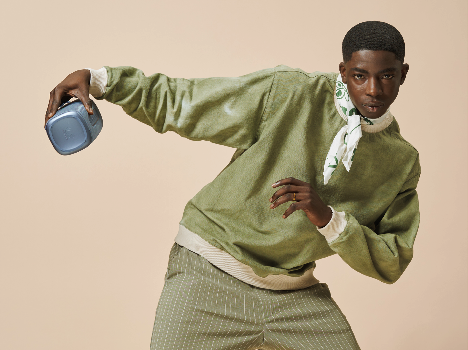 Man in groene kleding met een blauwe container, neutrale achtergrond.