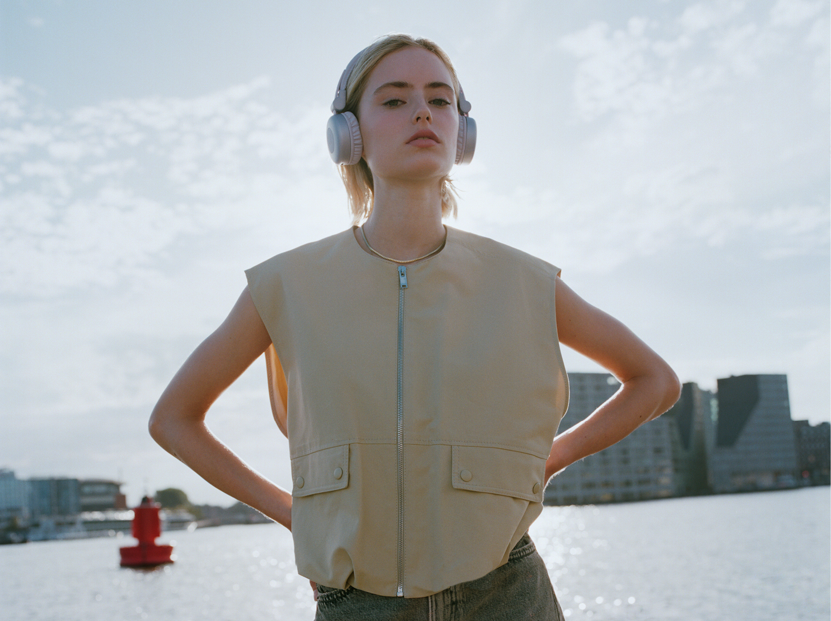 Femme avec un casque et un gilet debout dehors, mains sur les hanches. Ciel et eau.