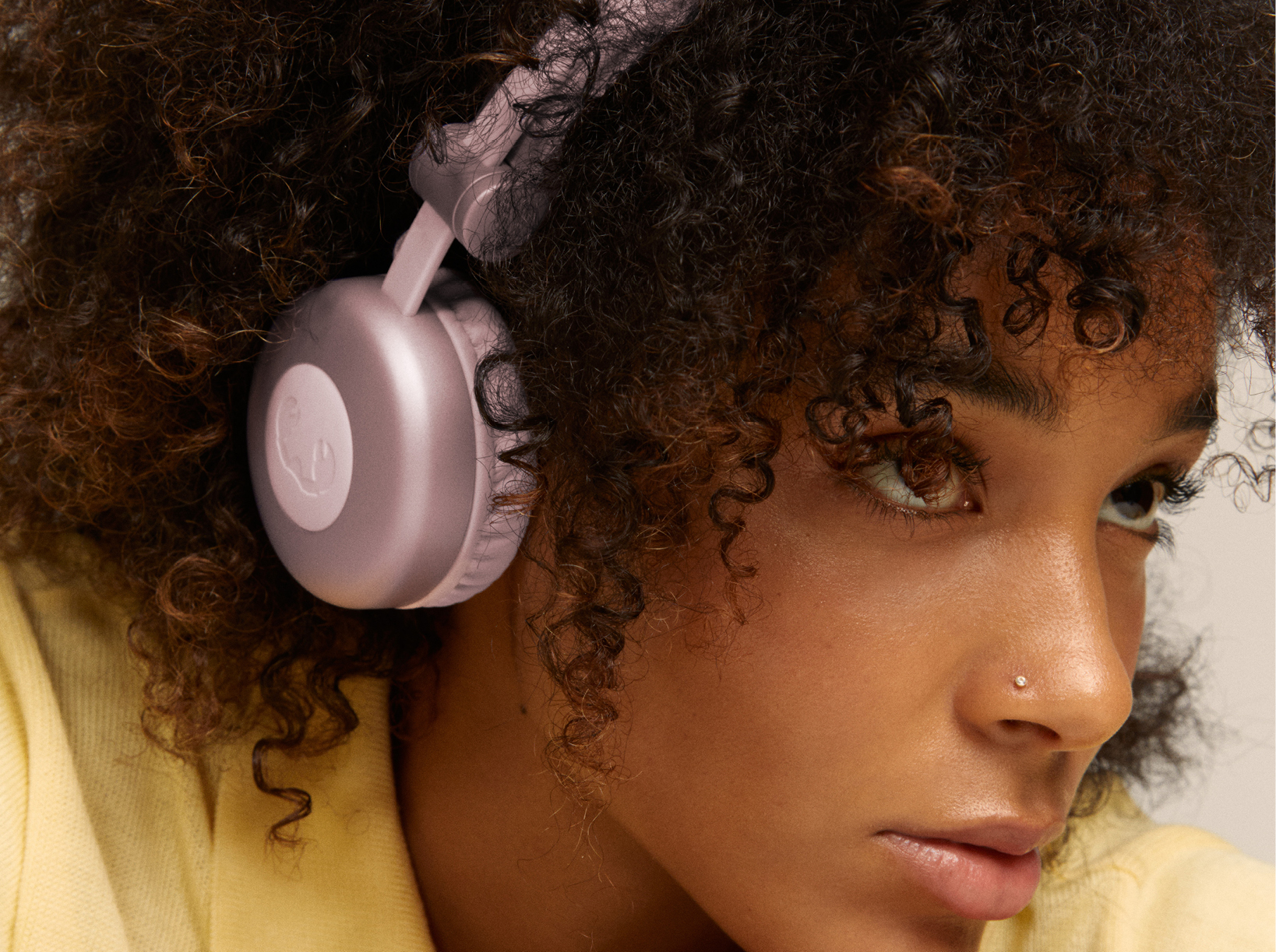 Femme aux cheveux bouclés portant un casque rose, gros plan, chemise jaune.
