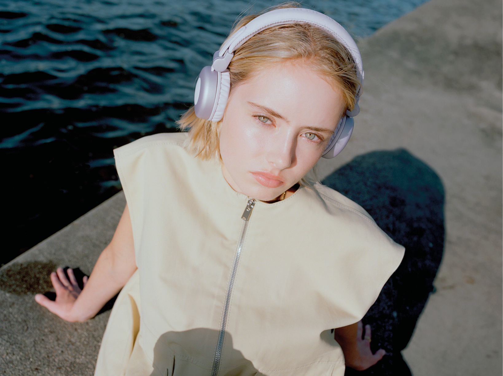 Une jeune femme portant un casque, assise près de l'eau, regardant le spectateur.