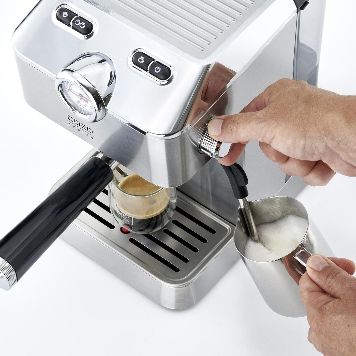 Eine Person, die eine silberne Espressomaschine benutzt und Milchschaum in ein Glas gießt.