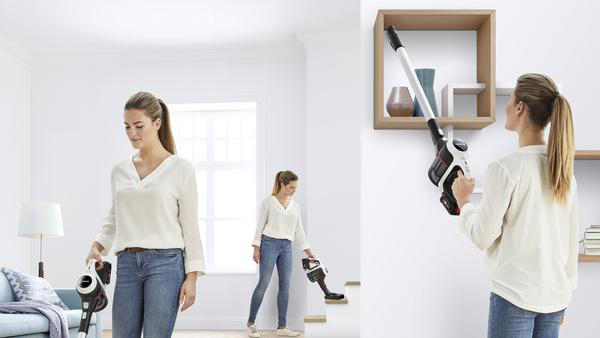 Frau staubsaugt, steht und auf Treppen, mit einem modernen kabellosen Staubsauger.