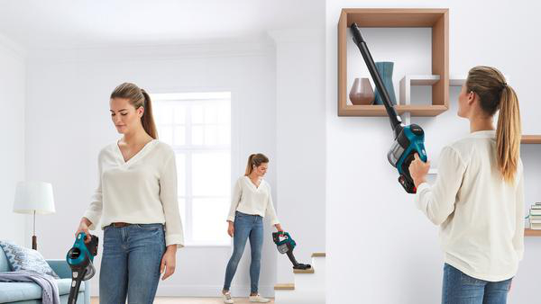 Frau benutzt einen Staubsauger in einem Wohnzimmer, auf Treppen und einem Regal.