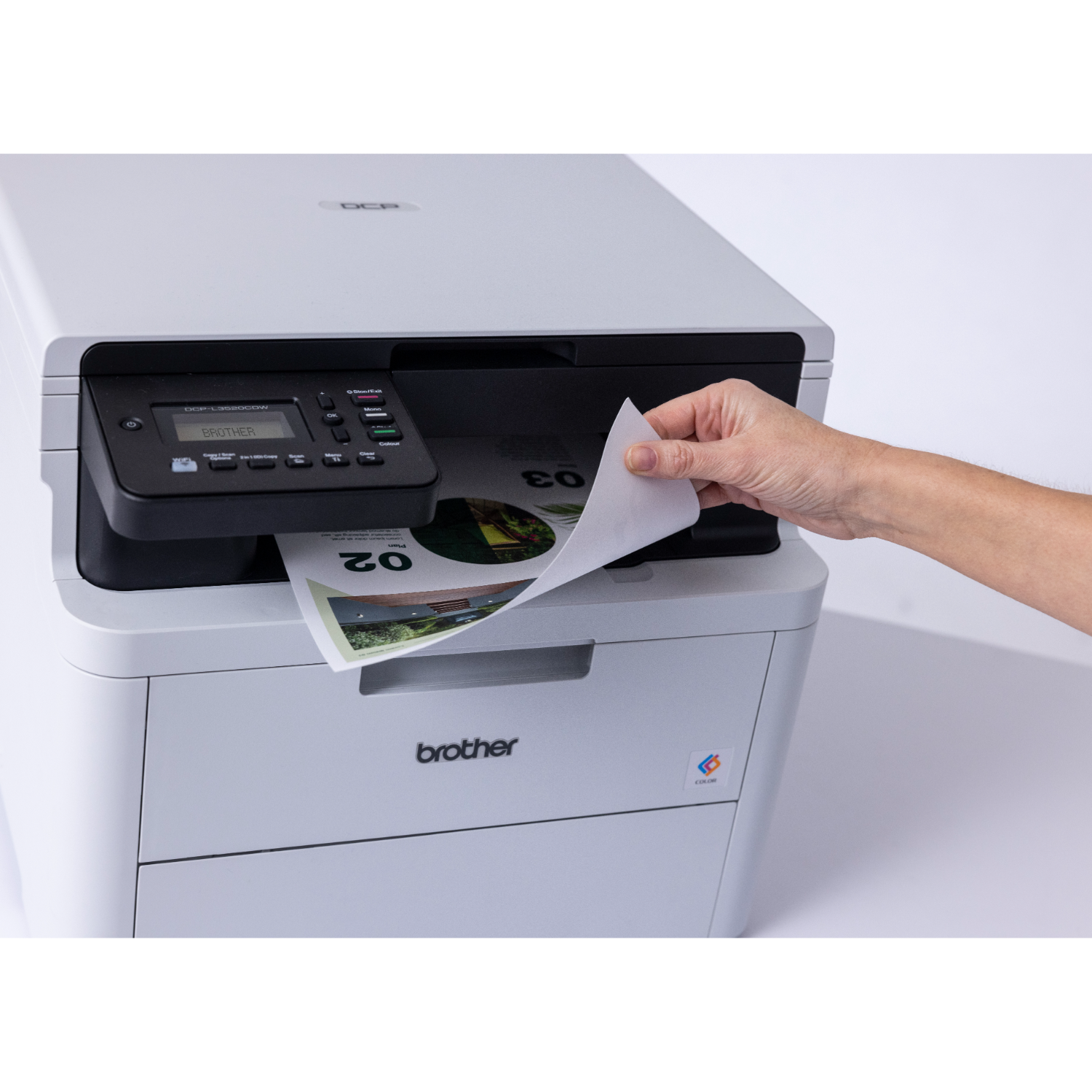 A person is pulling a printed paper from a white printer. The paper has '02' and '03'.